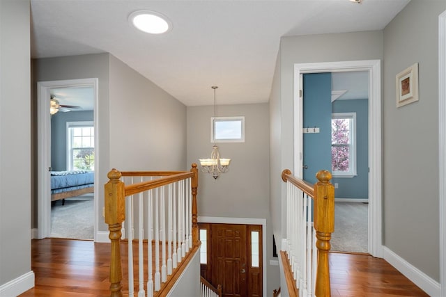 hallway with a chandelier, baseboards, an upstairs landing, and wood finished floors