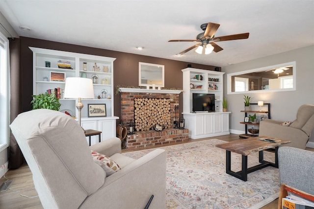 living room featuring plenty of natural light, a fireplace, a ceiling fan, and wood finished floors