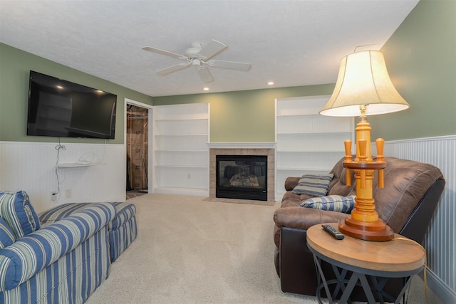 living area featuring a ceiling fan, a wainscoted wall, carpet flooring, and a tile fireplace