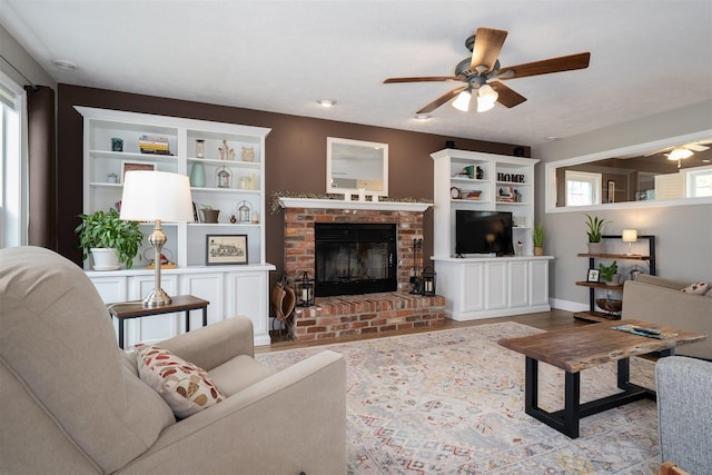 living area with a brick fireplace, a ceiling fan, baseboards, and wood finished floors