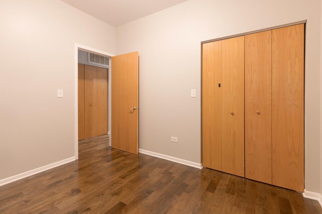 unfurnished bedroom with a closet, baseboards, and dark wood-style flooring