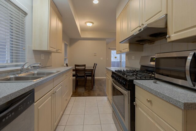 kitchen featuring light brown cabinets, stainless steel dishwasher, light tile patterned floors, a sink, and freestanding refrigerator
