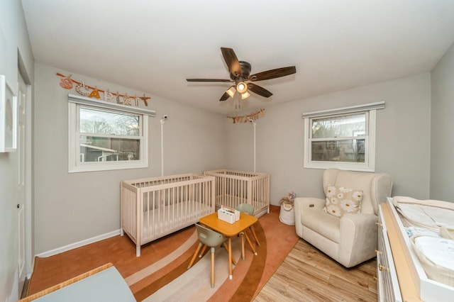 bedroom featuring a nursery area, wood finished floors, baseboards, and multiple windows