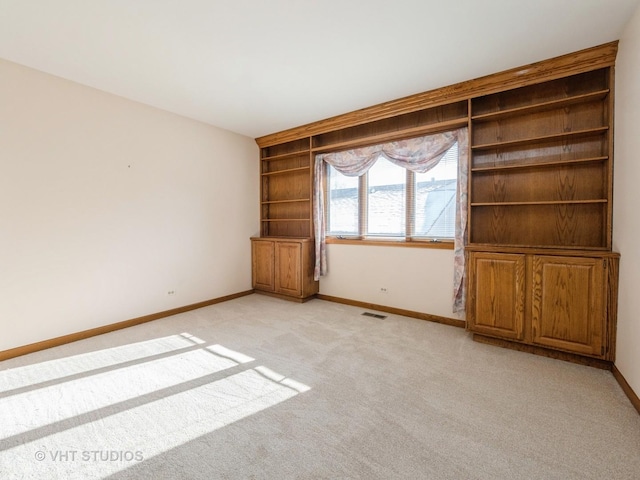 spare room featuring light colored carpet, baseboards, built in features, and visible vents