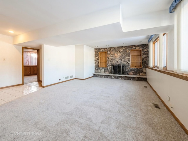 unfurnished living room featuring a stone fireplace, visible vents, carpet flooring, and baseboards