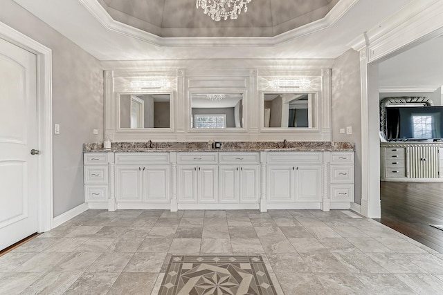 bathroom featuring a raised ceiling, baseboards, double vanity, and crown molding