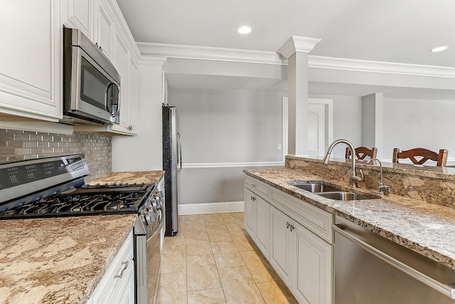 kitchen with appliances with stainless steel finishes, a sink, ornamental molding, white cabinets, and backsplash