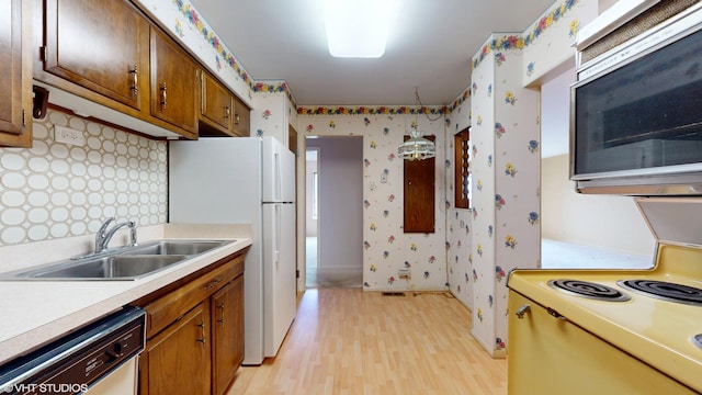 kitchen with wallpapered walls, light wood-style flooring, white appliances, and a sink