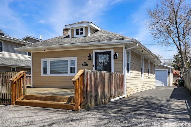 bungalow featuring an outbuilding, a detached garage, a deck, and a shingled roof