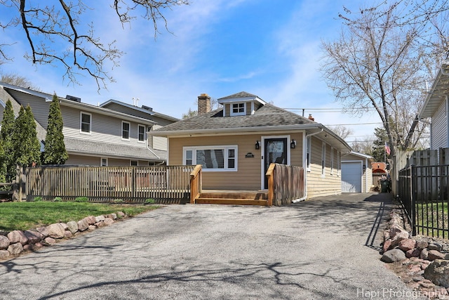 view of front of house featuring a wooden deck, an outbuilding, a detached garage, a chimney, and fence