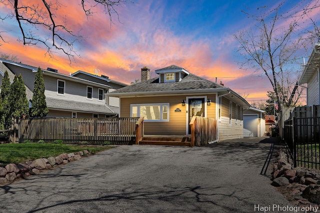 back of property at dusk with a garage, an outdoor structure, a chimney, a deck, and fence