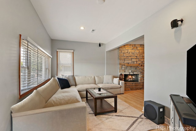 living area with light wood-style floors, visible vents, and a stone fireplace