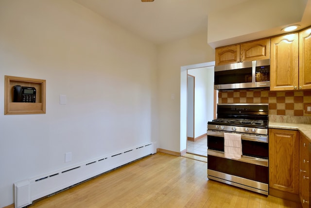 kitchen with stainless steel appliances, baseboards, decorative backsplash, a baseboard radiator, and light wood-style flooring