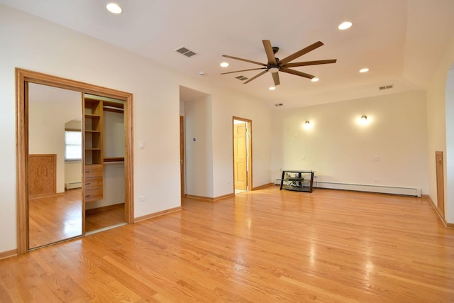 interior space featuring a baseboard heating unit, ceiling fan, visible vents, and light wood-style flooring