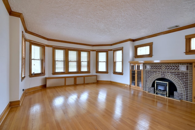 unfurnished living room featuring radiator, a tiled fireplace, visible vents, wood finished floors, and crown molding