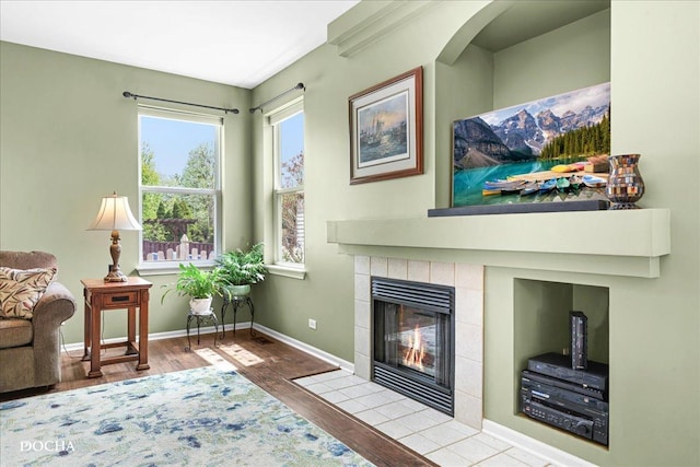 living area with baseboards, a tile fireplace, and wood finished floors