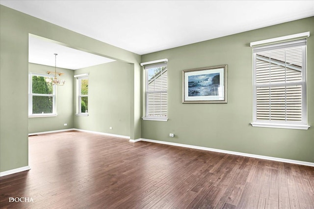 unfurnished room featuring dark wood-style flooring, baseboards, a chandelier, and a healthy amount of sunlight