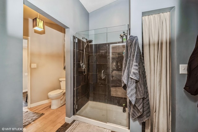 bathroom featuring toilet, wood finished floors, a shower stall, and baseboards