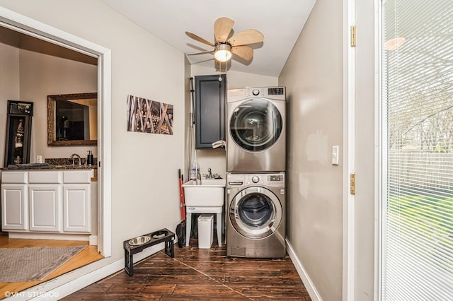 laundry area featuring baseboards, a ceiling fan, stacked washer / drying machine, and dark wood-type flooring