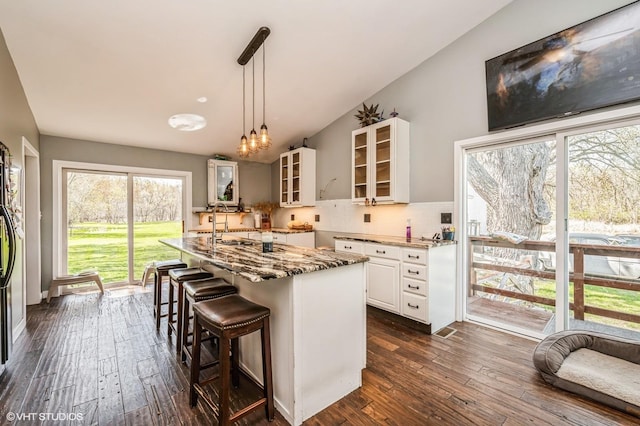 kitchen featuring dark wood finished floors, light stone countertops, glass insert cabinets, decorative backsplash, and white cabinetry