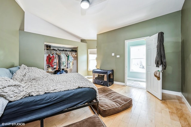 bedroom featuring baseboards, light wood-style floors, lofted ceiling, and a closet