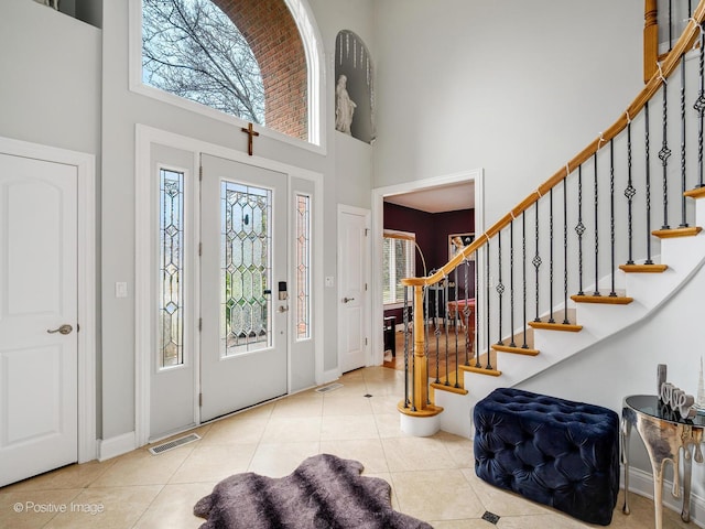 entryway featuring stairs, tile patterned floors, a towering ceiling, baseboards, and visible vents