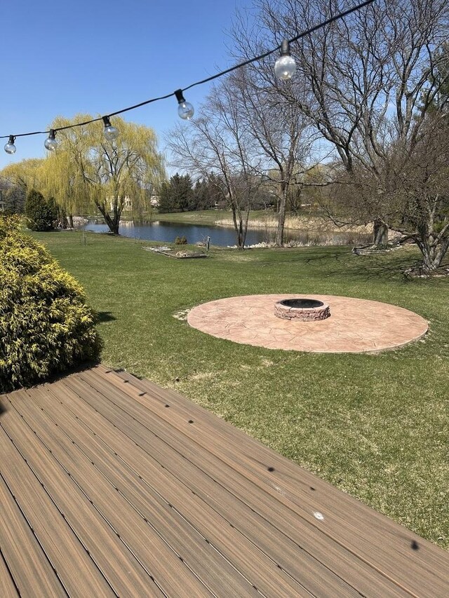 wooden terrace with a fire pit, a water view, a patio, and a lawn
