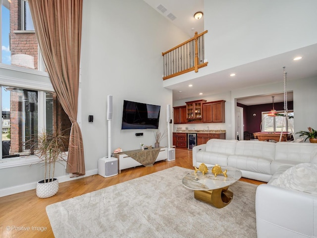 living area with light wood finished floors, indoor bar, wine cooler, a towering ceiling, and baseboards
