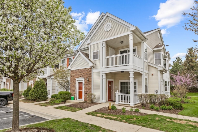 view of property featuring covered porch, uncovered parking, brick siding, and a balcony
