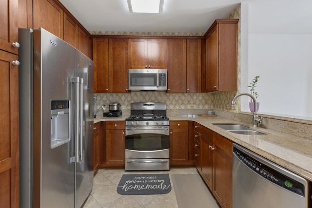 kitchen with a sink, stainless steel appliances, decorative backsplash, and light stone counters