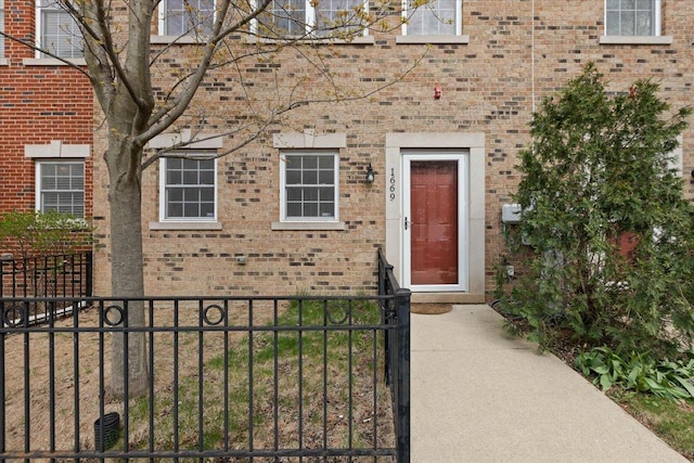 doorway to property featuring brick siding and fence
