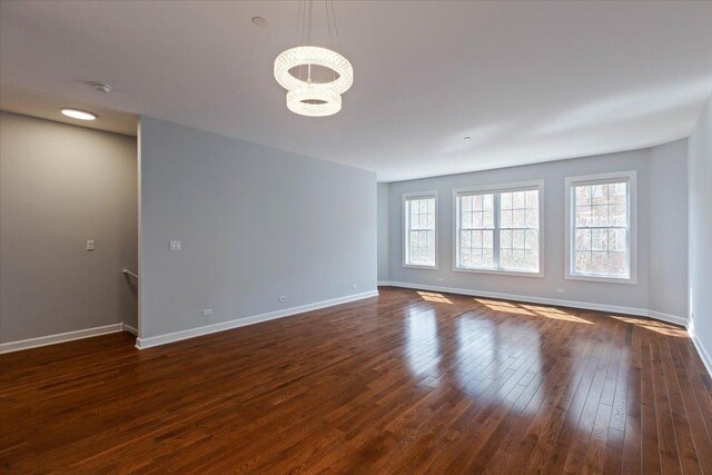 empty room with an inviting chandelier, dark wood-style floors, and baseboards