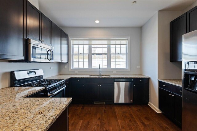 kitchen featuring recessed lighting, dark wood finished floors, stainless steel appliances, a sink, and light stone countertops