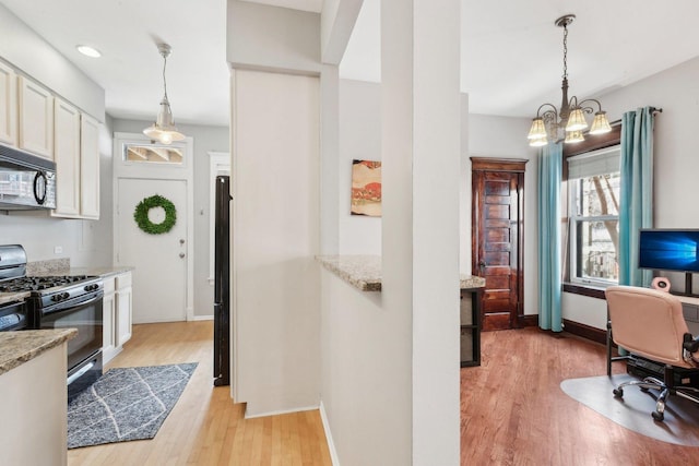 kitchen featuring light wood-type flooring, baseboards, white cabinets, black appliances, and a chandelier
