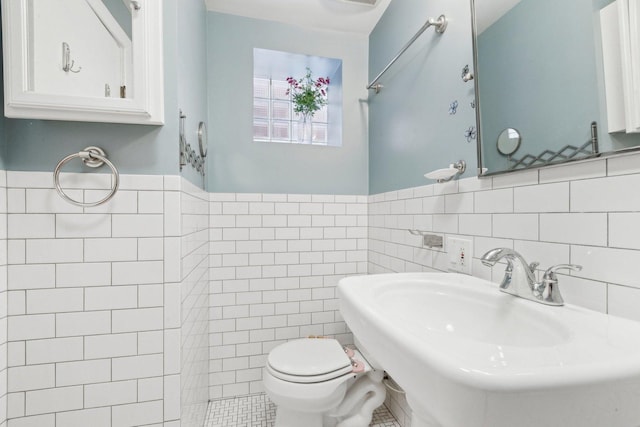bathroom with a sink, tile walls, wainscoting, and toilet
