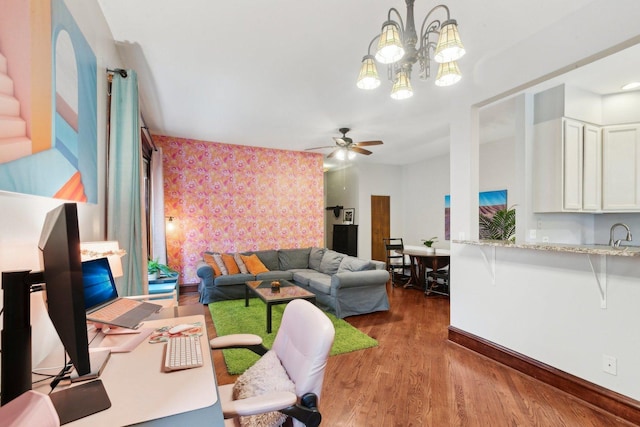 living area with baseboards, ceiling fan with notable chandelier, wallpapered walls, and wood finished floors
