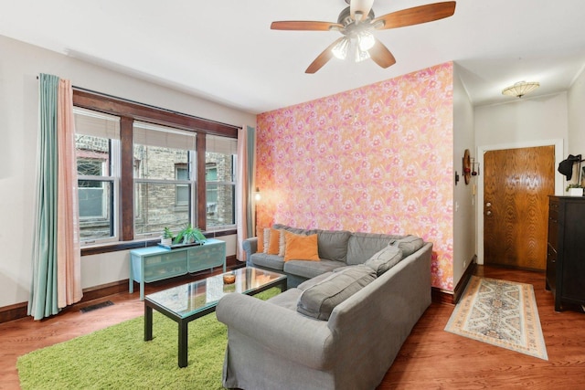 living area featuring a ceiling fan, baseboards, wallpapered walls, wood finished floors, and visible vents