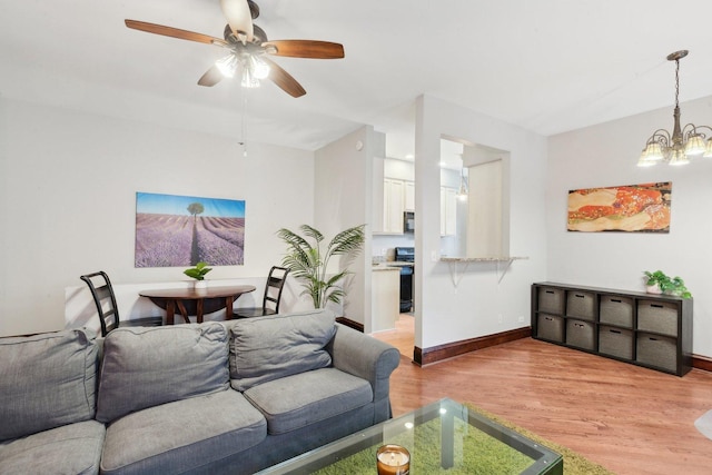 living area featuring light wood-style floors, baseboards, and ceiling fan with notable chandelier