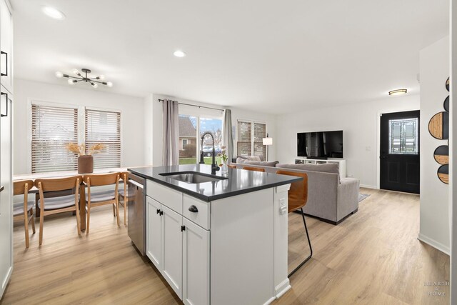 kitchen with white cabinets, a sink, dark countertops, light wood-style floors, and dishwasher