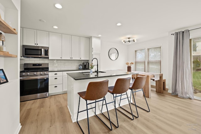 kitchen featuring stainless steel appliances, a sink, dark countertops, open shelves, and a breakfast bar