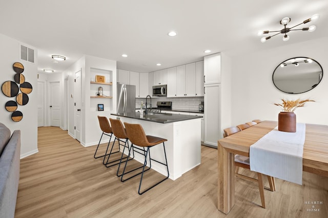 kitchen with dark countertops, a breakfast bar, light wood-type flooring, appliances with stainless steel finishes, and visible vents