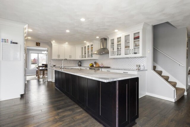 kitchen with white cabinets, a kitchen island with sink, dark wood-style floors, decorative backsplash, and wall chimney range hood