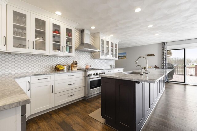 kitchen with wall chimney range hood, light stone counters, a sink, white cabinets, and high end stainless steel range oven