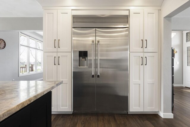 kitchen with white cabinets, stainless steel built in fridge, light stone countertops, and dark wood finished floors