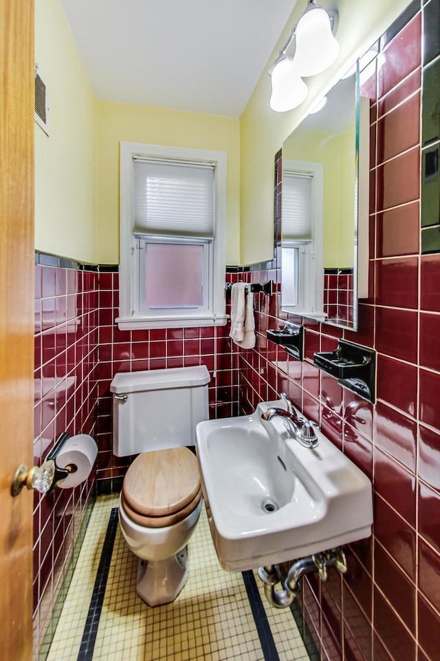 bathroom with tile patterned floors, visible vents, toilet, a sink, and tile walls