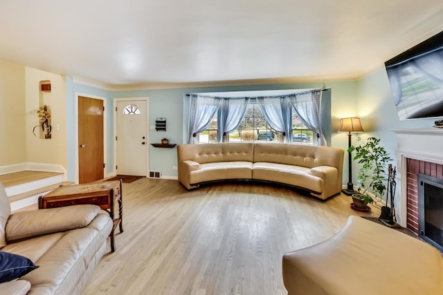 living area with a brick fireplace, wood finished floors, visible vents, and ornamental molding