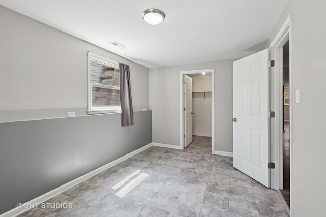 unfurnished bedroom featuring a walk in closet, visible vents, a closet, and baseboards