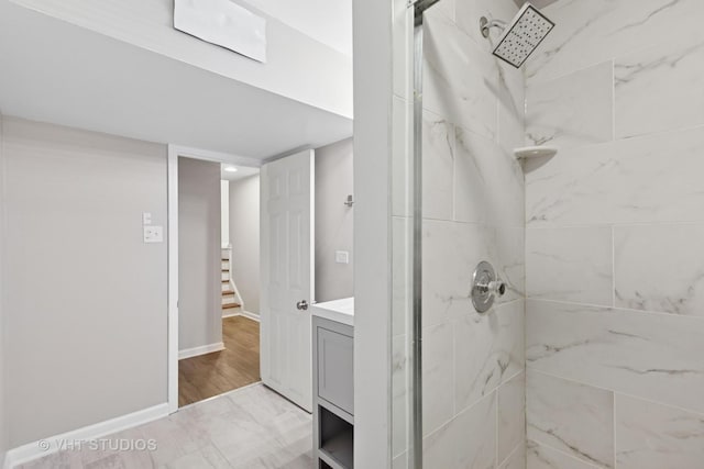 full bath featuring tiled shower, vanity, and baseboards