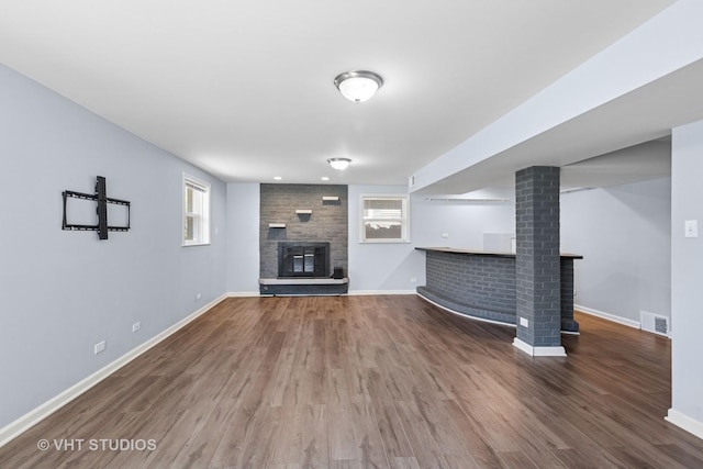 unfurnished living room featuring a brick fireplace, visible vents, wood finished floors, and baseboards