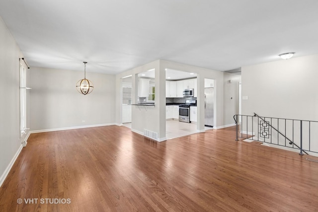 unfurnished living room featuring baseboards, a chandelier, and light wood-type flooring